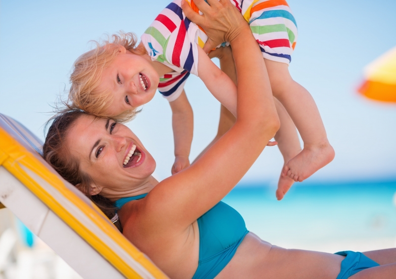 Mom holding up her child while smiling and wearing a bikini, showing her mommy makeover