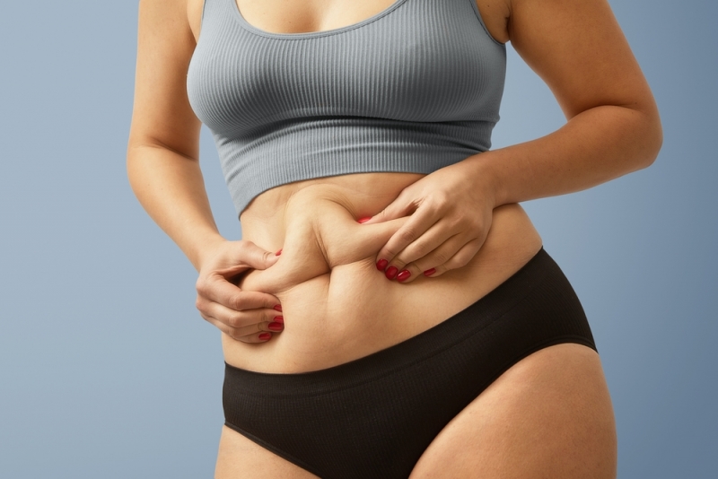 Woman in underwear and crop top pinching excess belly fat that she cannot lose in Scottsdale, AZ