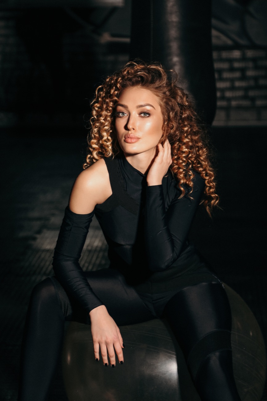Woman with curly red hair in a black bodysuit, seated